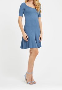 Pružné modré žebrované šaty s krátkými rukávy a rozšířenou sukní, doplněné o světle modré sandály na vysokém podpatku. Hladká textura.