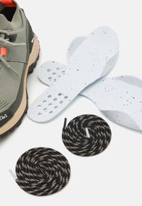 Scarpa sportiva verde con accenti grigi e rosa, due solette bianche macchiate e due lacci neri e bianchi a motivo avvolti nei dintorni.