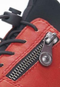 Red leather shoe with a textured finish, featuring a black fabric panel, laces, and a metallic zipper detail on the side.
