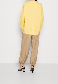 Gul överstor sweatshirt, beige baggy-byxor med elastiska manschetter och svarta strap-sandaler med rund klack.