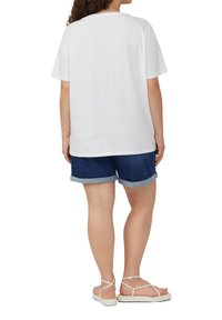 Witte katoenen T-shirt met korte mouwen, gecombineerd met donkere denim korte broek met opgerolde mouwen en beige sandaaltjes met straps, gezien vanuit de achterkant.