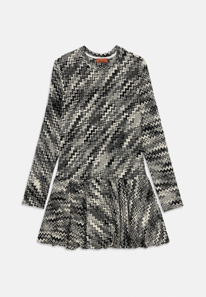 Vestido de mangas largas con patrón de zigzag en blanco y negro, cintura ajustada, escote redondo y falda acampanada sobre fondo blanco.