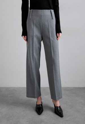Pantaloni gri croiți, cu o textură netedă, picior larg și pliuri frontale, asortați cu tocuri negre ascuțite și un top negru cu mânecă lungă.