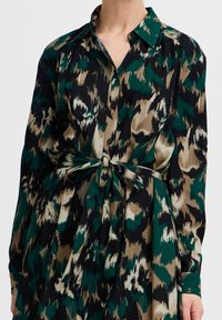 Abito camicia a maniche lunghe con un motivo astratto verde, beige e nero, chiusura con bottoni anteriori e vita regolabile grazie a un nodo.