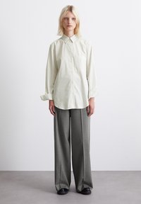 Striped, light green button-up shirt with a collar and pocket, paired with gray wide-leg trousers and black shoes. Sleek, tailored design.
