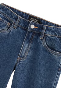 Jean en denim bleu foncé avec un design classique à cinq poches, fermeture à bouton argenté et surpiqûres orange contrastantes le long des coutures.