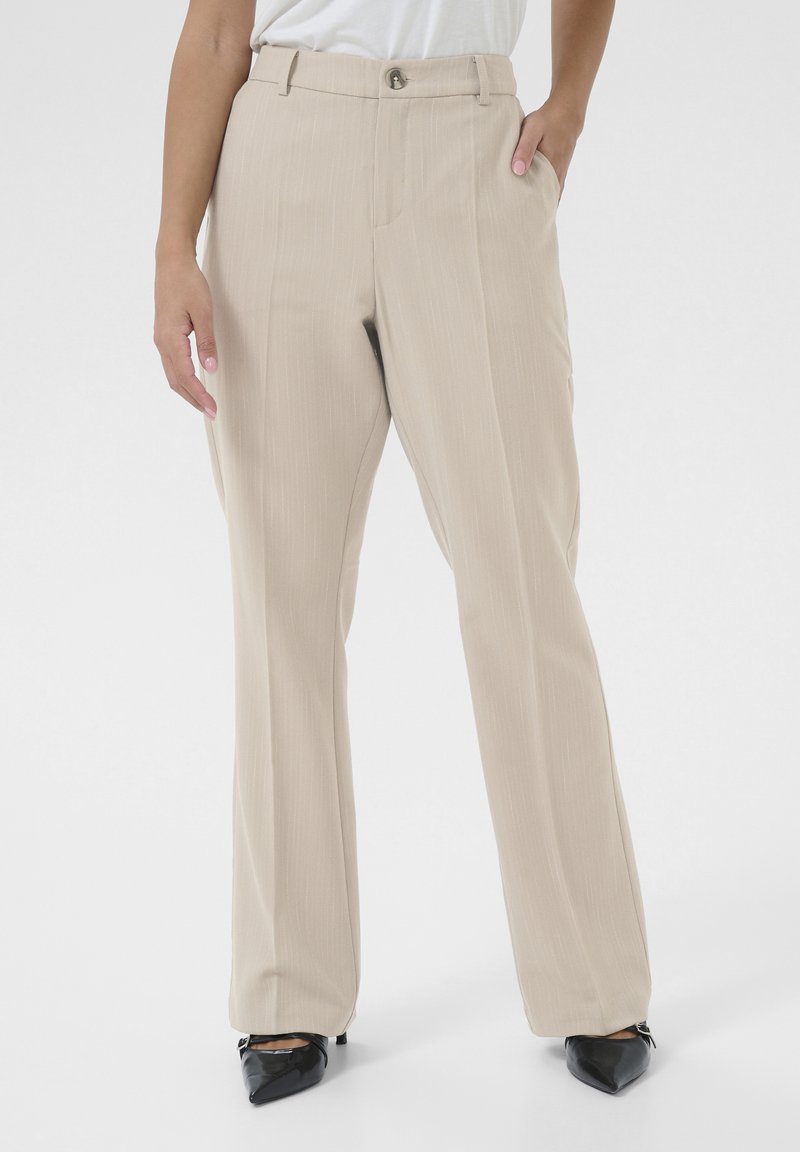 Beige gerade geschnittene Hose mit subtilen Streifen, ausgestattet mit einem vorderen Knopfverschluss und seitlichen Taschen, kombiniert mit schwarzen spitzen Absatzschuhen.