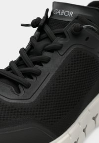 Chaussure de sport noire avec une tige en mesh texturé, semelle en caoutchouc et design à lacets. Présente un logo "Gabor" bien visible sur la languette.