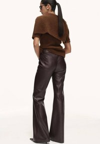Brown sweater with layered back design paired with dark brown faux leather flared pants, highlighting smooth texture and tailored fit.
