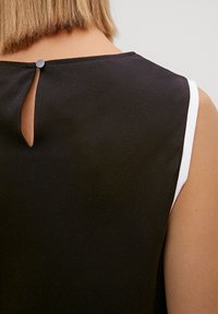 Schwarzes ärmelloses Top mit einem runden Ausschnitt, einem kleinen Schlüsselloch-Ausschnitt am Rücken und weißen Akzenten entlang der Armausschnitte. Angenehme, glatte Textur.