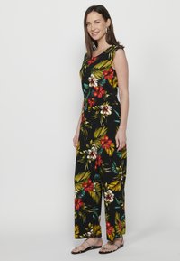 Accappatoio nero con vivaci motivi floreali in rosso, bianco e verde. Design senza maniche con una vestibilità morbida e pantaloni a gamba larga.