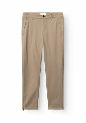 Beige slim-fit broek met steekzakken aan de voorkant, riemlussen, knoopsluiting en enkelsluitingen met rits, plat uitgevouwen op een witte achtergrond.