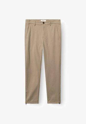 Pantalon beige ajusté avec poches avant, passants pour ceinture, fermeture par bouton et zips aux chevilles, posé à plat sur un fond blanc.