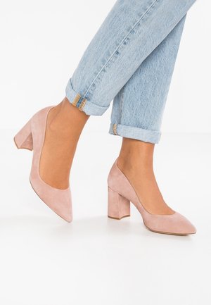 Escarpins en daim rose clair avec un talon carré block et un bout arrondi, portés avec un jean en denim bleu retroussé présentant des accents dorés.