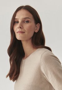 Pull beige clair avec un décolleté rond et des manches longues, fabriqué à partir d'un matériau tricoté doux, présentant un design minimaliste et une texture lisse.