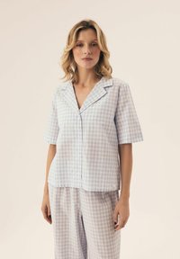 Jasnoniebieska i biała koszulka piżamowa z krótkim rękawem, z wyciętym kołnierzykiem, z przodem na guziki i miękkiego materiału; widoczne pasujące spodenki w kratkę.