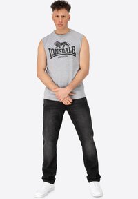 Grey sleeveless t-shirt with black LONSDALE logo; paired with dark jeans and white sneakers. Simple design and casual fit.