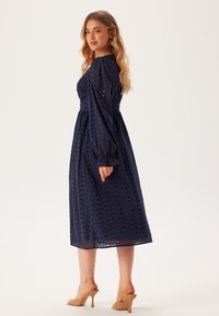 Marinblå midi-klänning med puffärmar och prickmönster. Lättviktig tyg med åtsittande bodice och lös kjol, kombinerad med tanfärgade klackar.