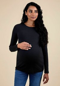 Fekete bordázott kismama felső hosszú ujjakkal és kerek nyakkivágással, kék farmernadrággal párosítva. Egy várandós személy látható, aki gyengéden tartja a hasát.