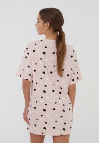 Abito t-shirt rosa con un motivo di piccoli cuori neri, bianchi e rosa. Maniche corte e una vestibilità oversize e rilassata.