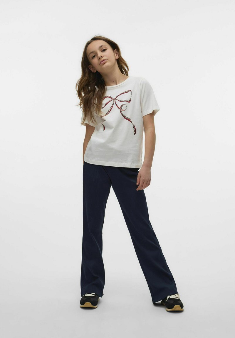 Vit bomullströja med ett röd och svart bandtryck på framsidan, tillsammans med mörkblå vida byxor och svarta sneakers.