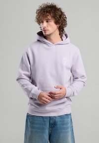 Vaalean lila huppari, jossa on etutasku ja valkoinen kukkakuosisekku. Mukana on nyörimyssy ja ribbikämmenet. Farkut täydentävät asun.