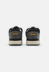 Black and gray sneakers with cream soles, featuring "GLOBE" branding on the heel and a textured panel along the sides.