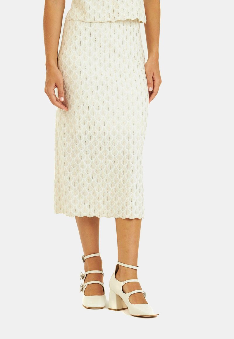 Strick-Midirock in Creme mit einem strukturierten Rautenmuster; kombiniert mit weißen Blockabsatzschuhen mit Fesselriemen und floralen Akzenten.