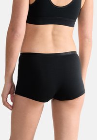 Sort bomuldstrusser med tætsiddende design og en blød elastisk talje, der har glatte kanter og minimale syninger for komfort.