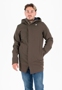 Giacca impermeabile marrone con cappuccio, zip frontale e due tasche laterali. Presenta un logo sul petto e una texture liscia e opaca.