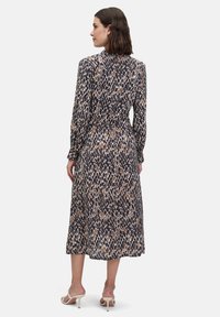 Długo rękawowa sukienka w kolorze granatowym, kremowym i brązowym, z wcięciem w talii i spódnicą o średniej długości. Gładki materiał z abstrakcyjnym wzorem.