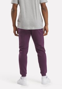 Purple joggers made from soft fabric with a tapered fit and ribbed cuffs, paired with a light gray t-shirt and white sneakers.