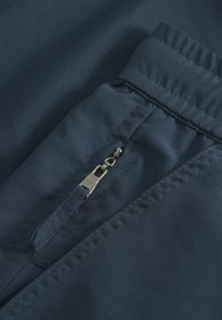 Marineblaue Stoff hat eine Reißverschlusstasche mit silbernem Beschlag. Glatte Textur mit Nahtdetails entlang der Kanten.