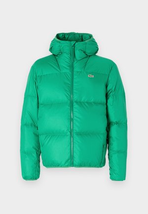 Zelena puhovka s kapuco, z zadrgo, prešitimi detajli in značilnim logotipom na levi prsni strani. Gladek, sijoč material.