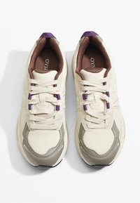 Béžové sieťované tenisky s fialovými akcentmi, okrúly špička, biele šnúrky a hnedé vnútorné podšívky. Obsahuje šedú gumovú podrážku a textúrovaný povrch.
