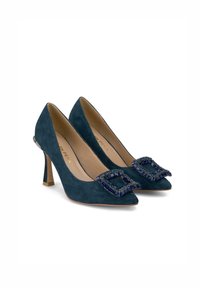 Scarpe con tacco alto in camoscio di un profondo verde teal con punta affilata. Presentano una fibbia decorativa abbellita con pietre blu.