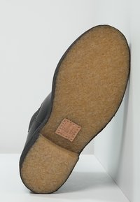 Suela de zapato negra con una superficie marrón texturizada, que presenta una etiqueta de cuero cosida en color marrón claro marcada "billi bi". Bisel curvado y acabado suave.