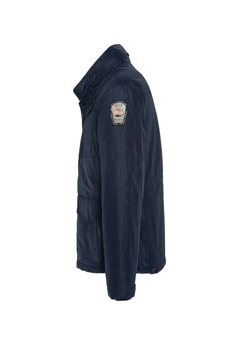 Giacca blu navy con chiusura zip, collo alto e tasche laterali. Presenta una patch sulla spalla sinistra con "19-23" e dettagli decorativi.