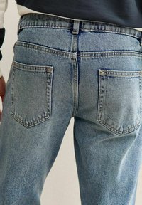Jeans de mezclilla azul claro con corte recto, que cuentan con dos bolsillos traseros y un sutil desgastado. Costuras visibles en los bolsillos y la cintura.