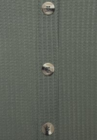 Tessuto a maglia verde testurizzato con righe verticali, caratterizzato da cinque bottoni circolari argentati lungo il pattino frontale.