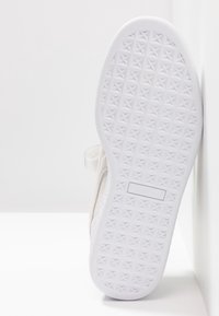Semelle blanche de basket avec motif diamant texturé et boîte rectangulaire de logo, reposant verticalement contre une surface blanche.
