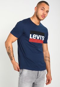 Camiseta de algodón azul marino con un audaz logotipo de Levi's en blanco y rojo sobre un fondo negro. Mangas cortas, escote redondo y un corte estándar.