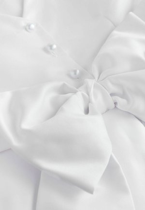 Weißer Satinstoff mit einer großen Schleifendetail. Drei Perlenknöpfe schmücken die glatte Oberfläche und zeigen eine weiche Textur und elegantes Design.