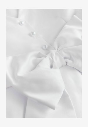 Biały satynowy materiał z dużą kokardą. Gładką powierzchnię zdobią trzy perłowe guziki, podkreślające miękką fakturę i elegancki design.