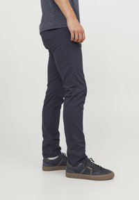 Jeans skinny azul marino con una textura suave, con costuras laterales y una cintura de altura media, combinados con zapatillas oscuras y calcetines blancos.