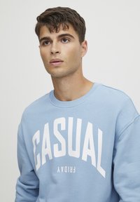 Svijetloplavi dukserica od pamučne mješavine s okruglim izrezom. Ima istaknuti bijeli natpis "CASUAL FRIDAY" na prednjoj strani.