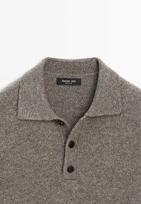 Szara dzianinowa koszulka polo z kołnierzykiem, trzema czarnymi guzikami i metką z napisem „Massimo Dutti”, prezentująca gładką, teksturowaną tkaninę.
