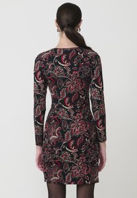 Vestido de manga larga en tejido negro con un colorido estampado de flores paisley en rojo, crema y verde. Silueta ajustada con escote redondo.