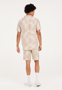 Camisa de manga corta beige y pantalones cortos a juego con un estampado de hojas blancas, textura similar al algodón, llevados con calcetines blancos y zapatos de color claro.