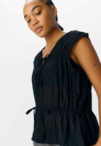 Top negro con plisados, mangas cortas, escote en v y cintura con cordón ajustable. Tejido ligero con una textura suave y diseño fluido.